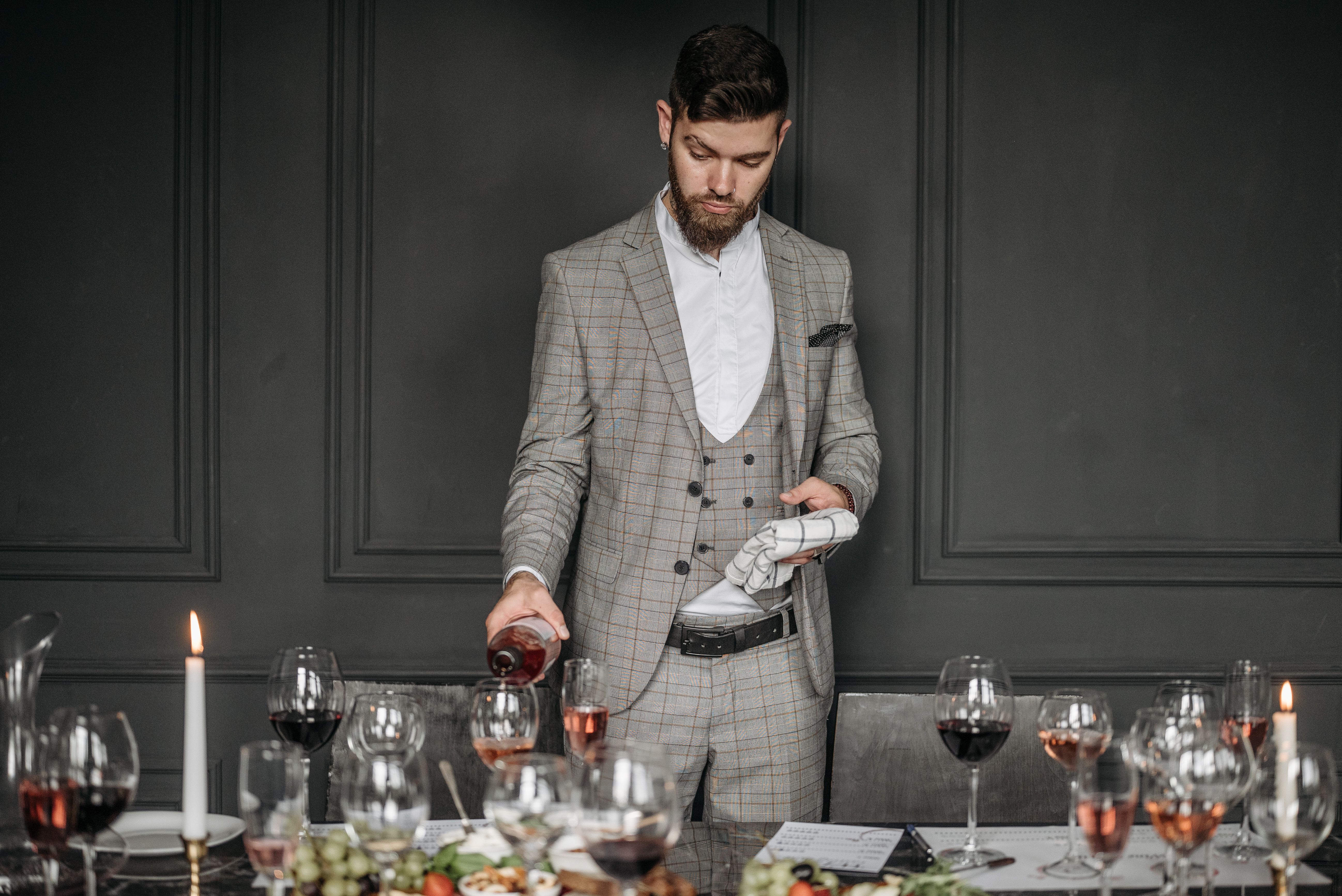 A sommelier pouring red wine at an elegant dinner table, reading the room's timing and mood