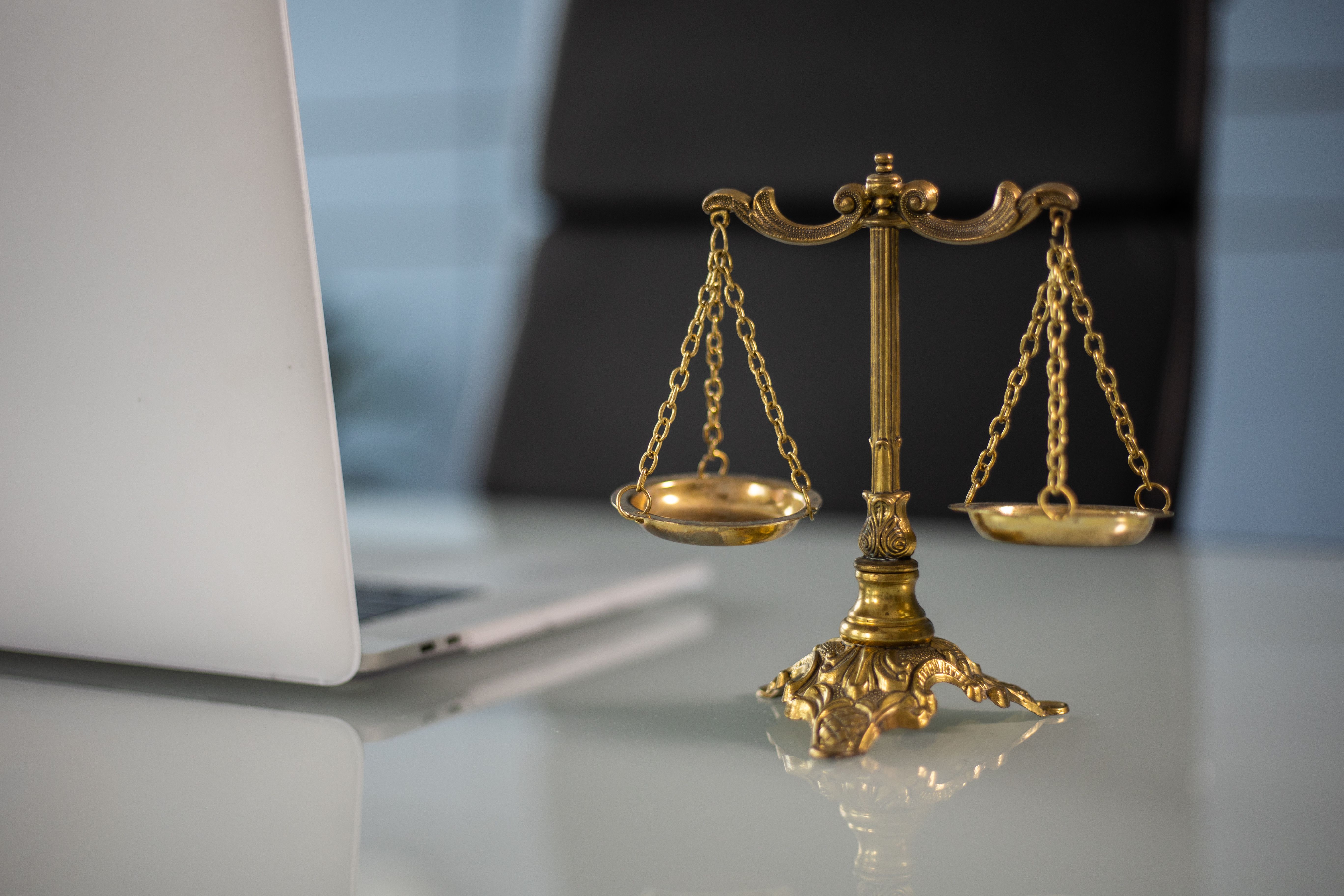 Golden scales of justice on a desk beside a laptop in a modern law office